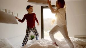 Two children have a pillow fight on their bed, ignoring their night routine.